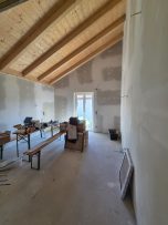 Innenraum eines noch unvollendeten Raums mit Holzdecke und Baustellenmaterialien.